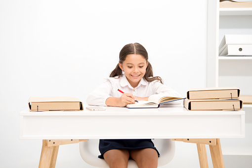 Excellent pupil. Girl child writes hometask while sit table white background. Schoolgirl studying writing essay. Kid girl school uniform happy face does exercise hometask, copy space.