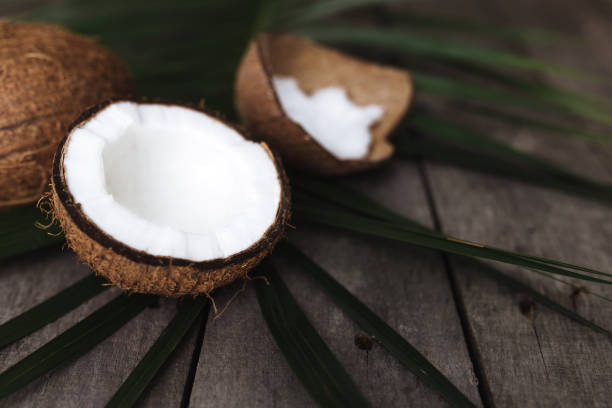 istock Broken coconuts on gray wooden background with palm leaf. White coconut pulp 1306306859