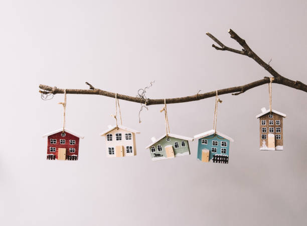 Beautiful festive new year and Christmas decorative little wooden houses hanging on a stick on the grey wall background, with fireflies glowing on the foreground stock photo