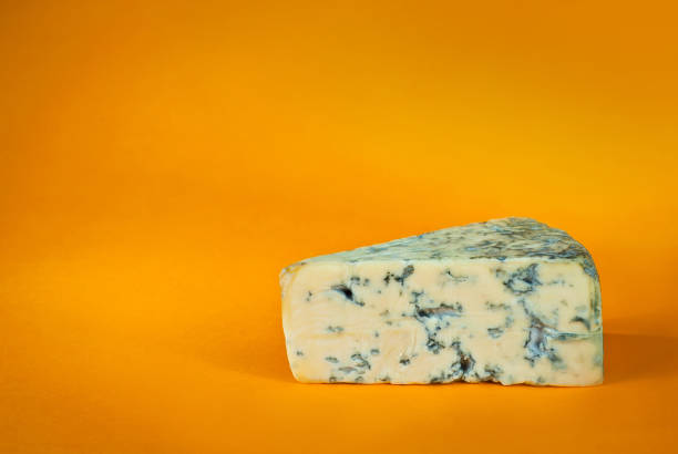 istock Yellow piece of cheese on an orange background. Triangular cheese with mold close up. Copy space and free space for text near the cheese. 1306310679