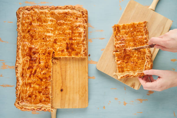 A person cuts portions of a freshly baked patty with natural ingredients such a tomato, onion, pepper, tuna, egg and dough of wheat. Tuna pie. Typical Galician dish from Galicia and Spain stock photo