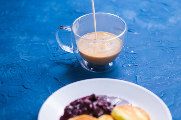 frühstück und leckeres konzept - pfannkuchen aus hüttenkäse mit marmelade, blauem hintergrund. kaffee in eine tasse gießen. - cheesecake syrup cottage cheese cream stock-fotos und bilder