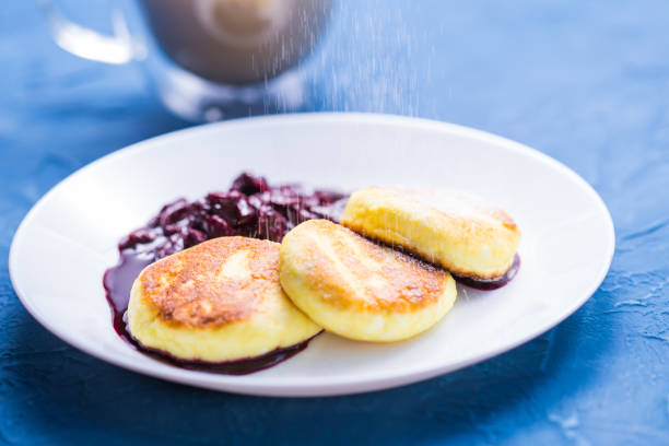 frühstück und leckeres konzept - pfannkuchen aus hüttenkäse mit marmelade, blauem hintergrund. mit puderzucker bestreuen. - cheesecake syrup cottage cheese cream stock-fotos und bilder