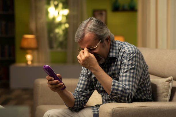 shot of Mature man sitting on sofa watching tv- stock photo Mature Men, Watching TV, 50-59 Years, Adult, adult only, India, Indian ethnicity, cross match stock pictures, royalty-free photos & images