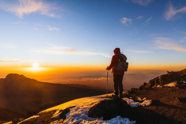 Man hiker achieved the dream enjoying the awe sunrise from the top of Kilimanjaro mountain Man with backpack and hiking poles got to the top of Africa - Mount Kilimanjaro and looking at the beautiful bright sunny sunrise above the Meru mountain natural landmark stock pictures, royalty-free photos & images