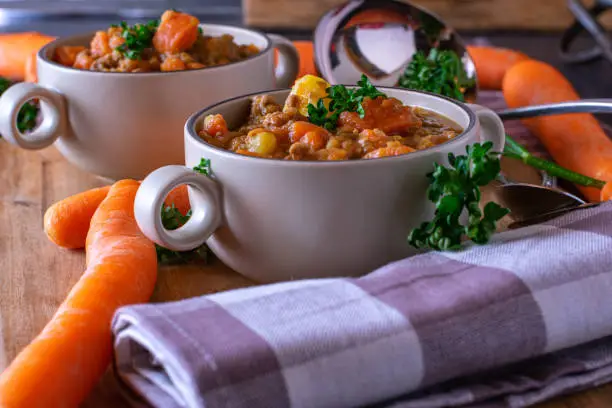 Delicious carrot stew with minced meat, potatoes and lentils served in rustic soup cups on wooden table background. Ready to eat