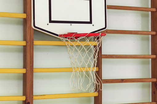 Basketball metal hoop hanging on wooden ladder in children gym during physical culture lesson