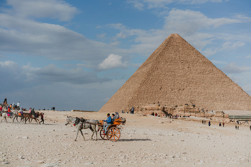The Sphinx stands tall with the Great Pyramid in the distance in Giza Egypt under blue sky