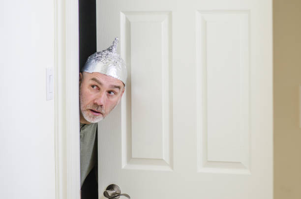 man with aluminum foil hat behind door - tin foil hat imagens e fotografias de stock