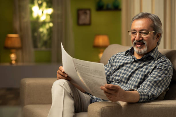istock Mature Man Reading Papers While Sitting On sofa At Home:- stock photo 1306318103