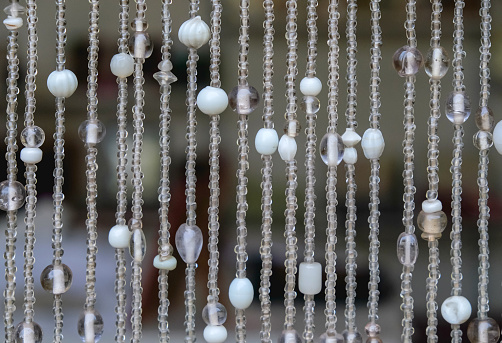 Close-up details shot of beaded curtains as room dividers. There's variation size of glass seed beads, in white, beige, and transparent color.