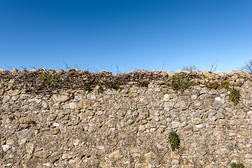 Close-up of a boundary wall made of stones and concrete in the countryside with clear blue sky on background. Garda, Verona province, Veneto, Italy, Europe.