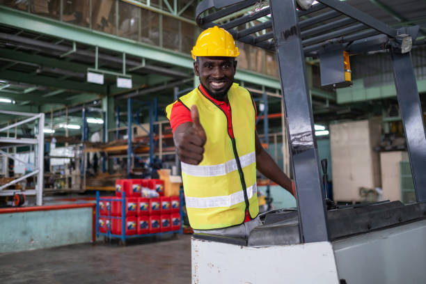 istock Confident African engineer or technician worker wearing safety helmet and vest standing on the forklift and thumb up and smile in the automotive part warehouse. Happy work in the inventory factory 1306325400