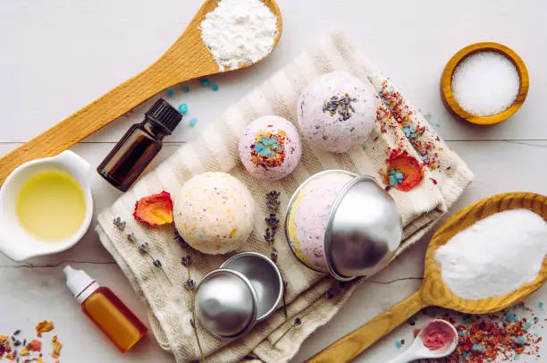 Photo of Making bath fizz bombs at home concept. All the ingredients on table on wood spoons: cornstarch, essential oil, dye, citric acid, baking soda, dry herbs, round metal pressing molds.