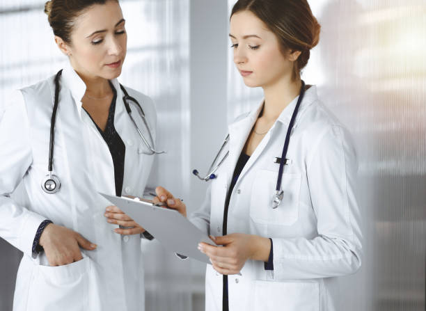 istock Two female physicians are discussing their patient's medical tests, while standing in a sunny clinic office. Doctors use a clipboard at work. Teamwork in medicine 1306327197