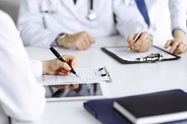 istock Group of unknown doctors are sitting at the desk and discussing problems or disease treatment in modern hospital office. Coronavirus countering, patient help in medicine concept 1306329363