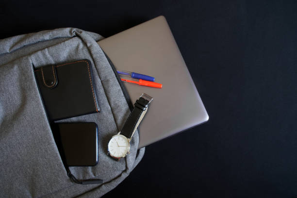 istock A small urban gray textile backpack with a laptop or ultrabook, a wallet, a smartphone and a wristwatch lies on a black background. Attributes of an urban traveler, programmer or student 1306329456