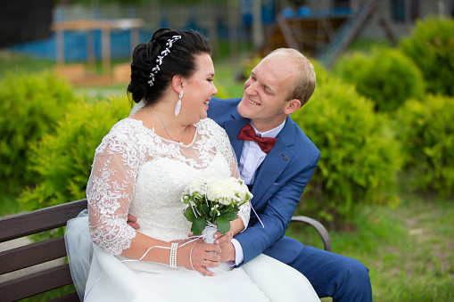 The fat bride and the thin groom sit on the bench and talk to each other.