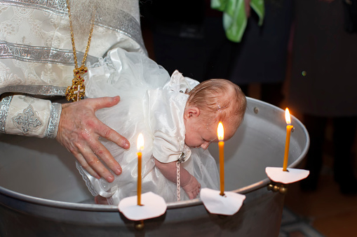 Orthodox rite of baptism of a child. The hands of the priest bathe the baby in the baptismal bath.