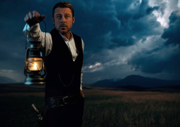 Man in victorian clothing with lantern standing on prairie area.
