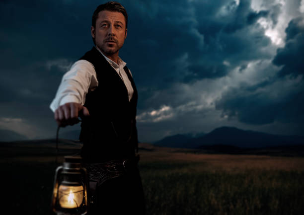 istock Man in victorian clothing with lantern standing on prairie area. 1306333605