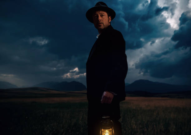 istock Man in victorian cowboy clothing with lantern standing on prairie area. 1306333621