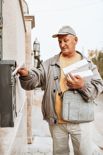 Senior Mailman Carrying Boxes And Delivering Letters To Mailbox