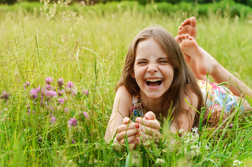 girl of 10 years old lies on the grass among the flowers and laughs