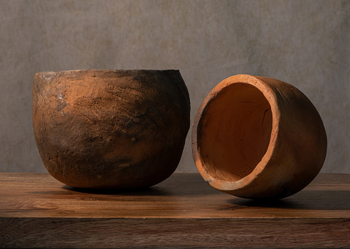 Two simple, rustic, hand-made pottery with clay, fire-burnt, to hold water or cook, on wooden background, brown, two pieces, side view