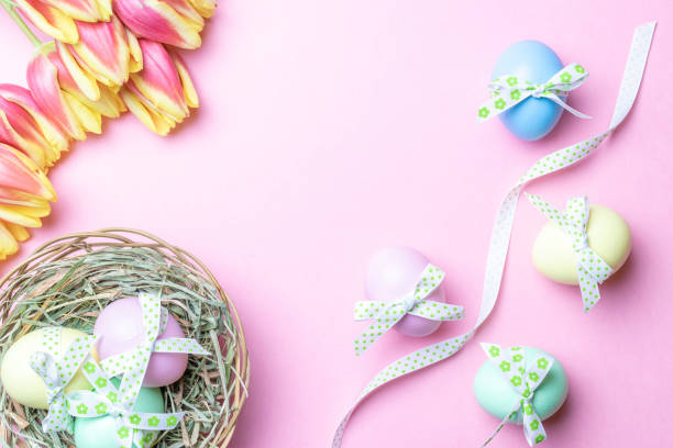istock Basket easter decoration: Colourful egg with tape ribbon, spring tulips, white feathers on pastel pink background. Congratulatory easter design. Top view. 1306339762