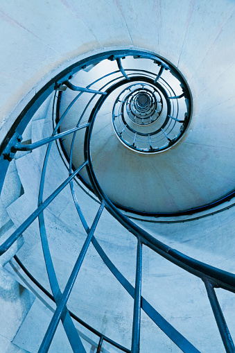 Old-fashioned spiral stairs in Arc de Triomphe in Paris – France  . Blue filter and low angle shot.