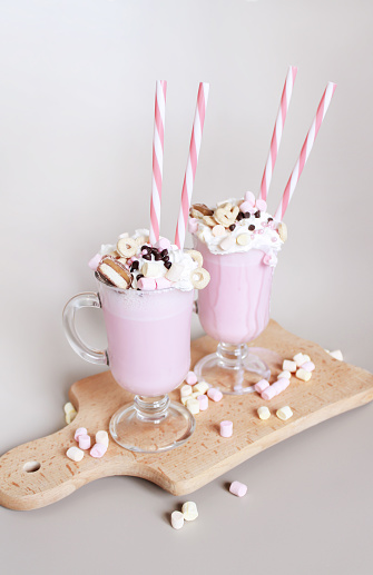 Two pink milkshakes or freakshakes with whipped cream, marshmallows, sprinkles and straws