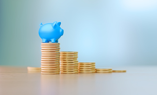 Blue piggy bank sitting on coins before defocused background. Horizontal composition with copy space. Great use for saving and investment concepts.