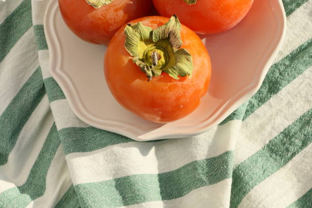istock Fresh ripe persimmons on a white plate with a classic design on a green-white striped tablecloth, Paradise Palms 1306344905