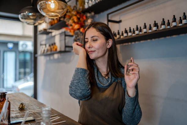 Young Perfumer preparing perfume while sitting at table in her own store Young Perfumer preparing perfume while sitting at table in her own store perfume counter stock pictures, royalty-free photos & images