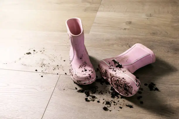Photo of dirty muddy kids rubber rain boots on laminate floor