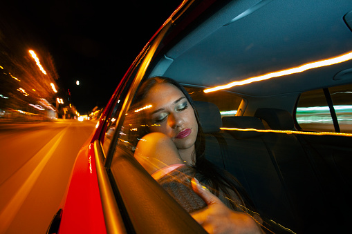 Beautiful woman sleeping in a car in motion - urban city scene with motion blur. About 20 years old, Caucasian brunette.