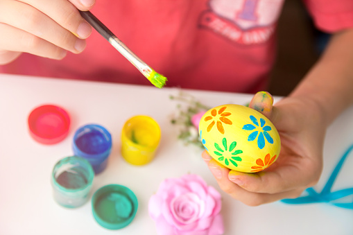 Close up of children's hands holding Easter egg and painting brush. Preparing for Easter. Children paint Easter eggs with colors.