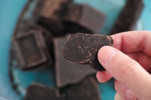A man holding a piece of homemade broken dark chocolate in his hand. Close up.