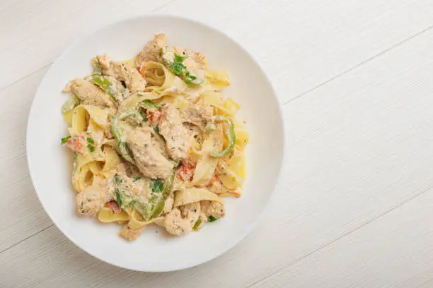 Photo of Cajun chicken Fettuccine pasta in a creamy sauce on white plate. Top view.