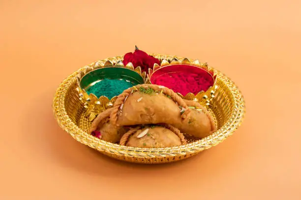 Ornamental Golden Thali Decorated With Exotic Indian Dessert Gujia Or Gujiya Mithai And Colorful Gulal Abeer Or Abir For Happy Holi Festival Celebration Isolated On Beige Background With Copy Space
