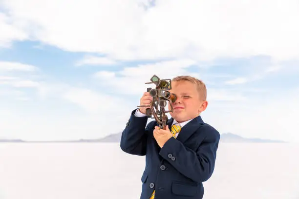 A young business boy looks through a telescope searching for new business opportunities. He is standing on the Bonneville Salt Flats, in Utah, USA. New ideas sometimes take you outside the box.