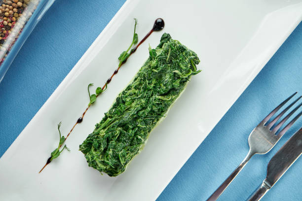 istock Delicious side dish for main courses - stewed spinach in cream in a white plate on a blue tablecloth 1306350833