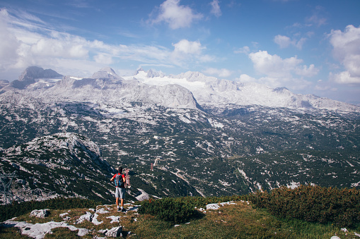 dark-skinned man with a backpack on his back looks at the Dachstein massif in Upper Austria. A purposeful boy in sportswear enjoys nature on the Krippenstein mountain
