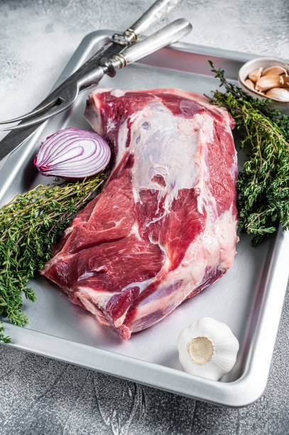 istock Raw lamb or goat shoulder meat in a baking dish with knife and meat fork. White background. Top view 1306355546