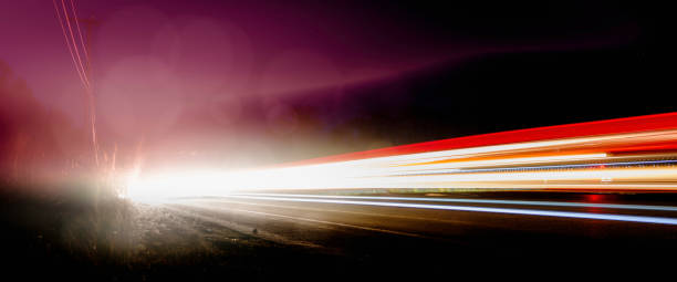 bright car light trails et bokeh effects on foggy night highway. fond de nuit de mouvement de vitesse. faisceaux lumineux blancs rouges voyageant de gauche à droite. plan rapproché horizontal panoramique avec l’espace noir pour le texte ou la conceptio - multiple lane highway flash photos et images de collection