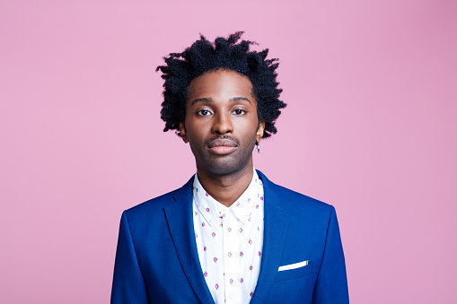 Confident afro american man wearing blue jacket and white shirt, looking at camera. Studio shot on pink background. Portrait of designer.
