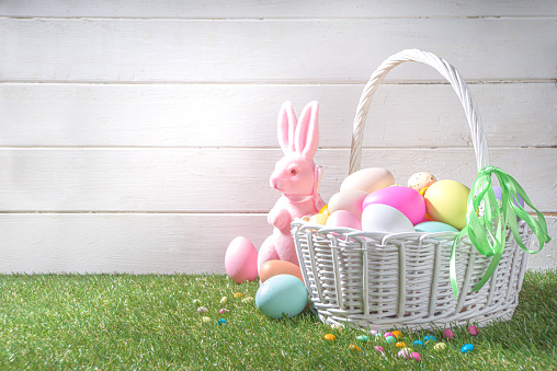 Easter background. Vase with a bouquet of tulips flowers, Easter eggs and bunny rabbits decor. On white wood kitchen table backdrop copy space