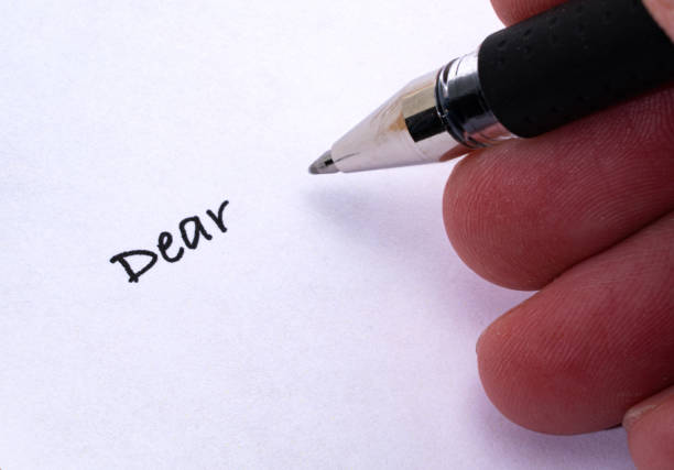 The photo is taken indoors out of a personal perspective with copy space. A woman is writing words of a speech on white paper.