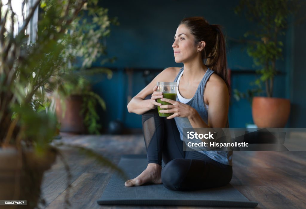 Mujer en forma bebiendo un batido de desintoxicación verde en el gimnasio - Foto de stock de Estilo de vida saludable libre de derechos